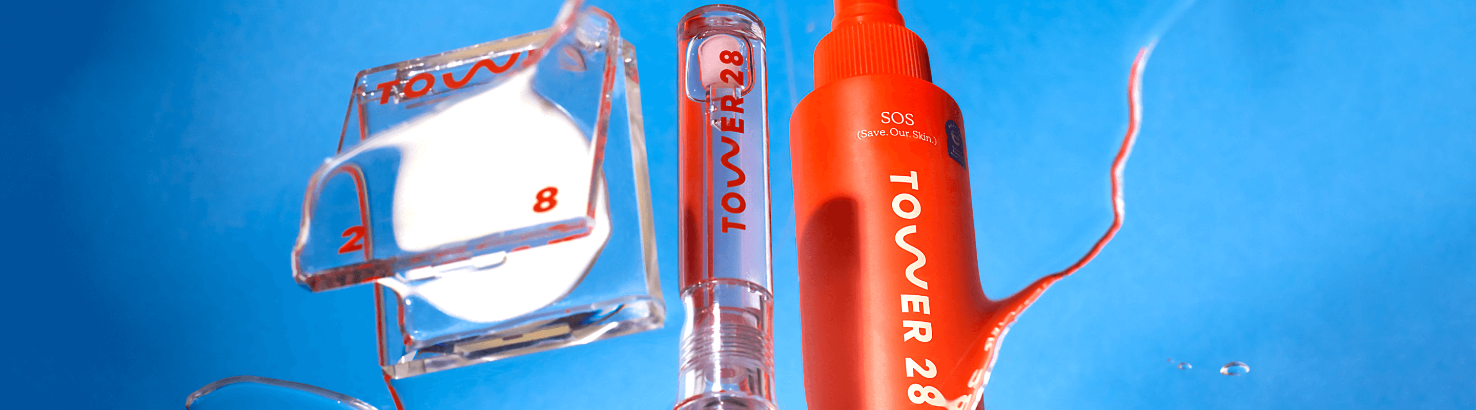 [A reflection of Tower 28 Beauty's SuperDew Highlight Balm, ShineOn Lip Jelly, and SOS Rescue Spray on a blue background.]