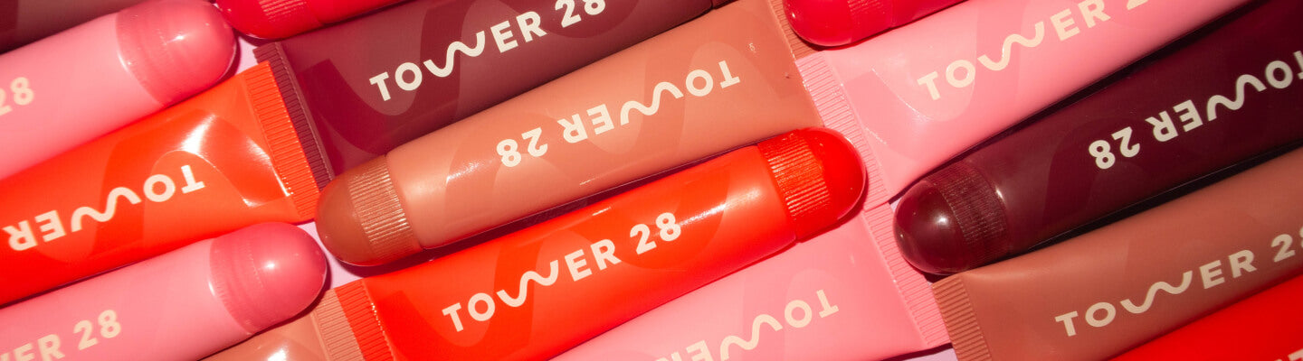 Tower 28 Beauty Holiday Drip 2023 Collection Flatlay of Lip Drip Duo, Tower 28 x DEUX Cookie Butter Drip on a wooden chair.