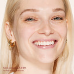 Close-up of a woman's face with blonde hair and gold hoop earrings, wearing a light makeup look. [1.0 BH]