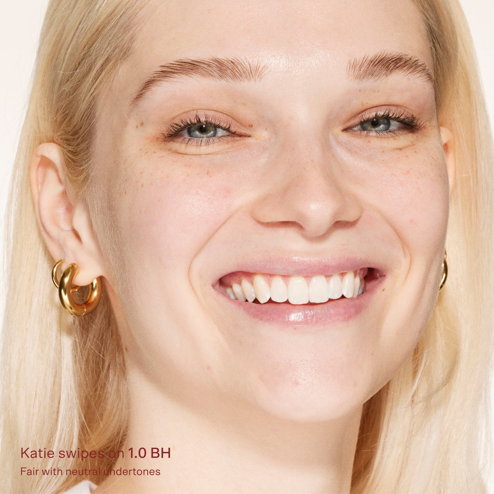 Close-up of a woman's face with blonde hair and gold hoop earrings, wearing a light makeup look. [1.0 BH]