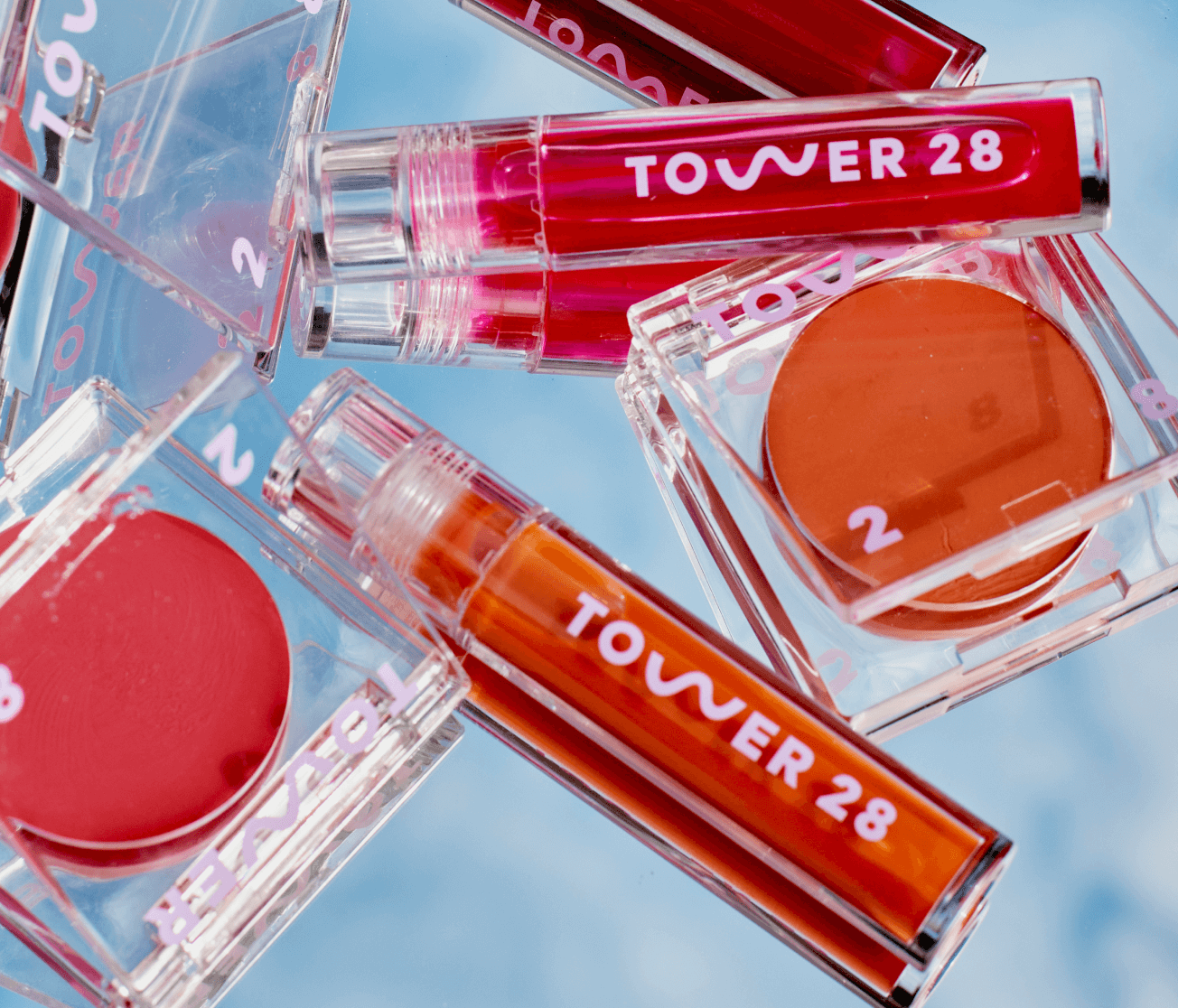 [A close of up of the Tower 28 Beauty BeachPlease Cream Blush and ShineOn Lip Jelly on a mirror surface.]