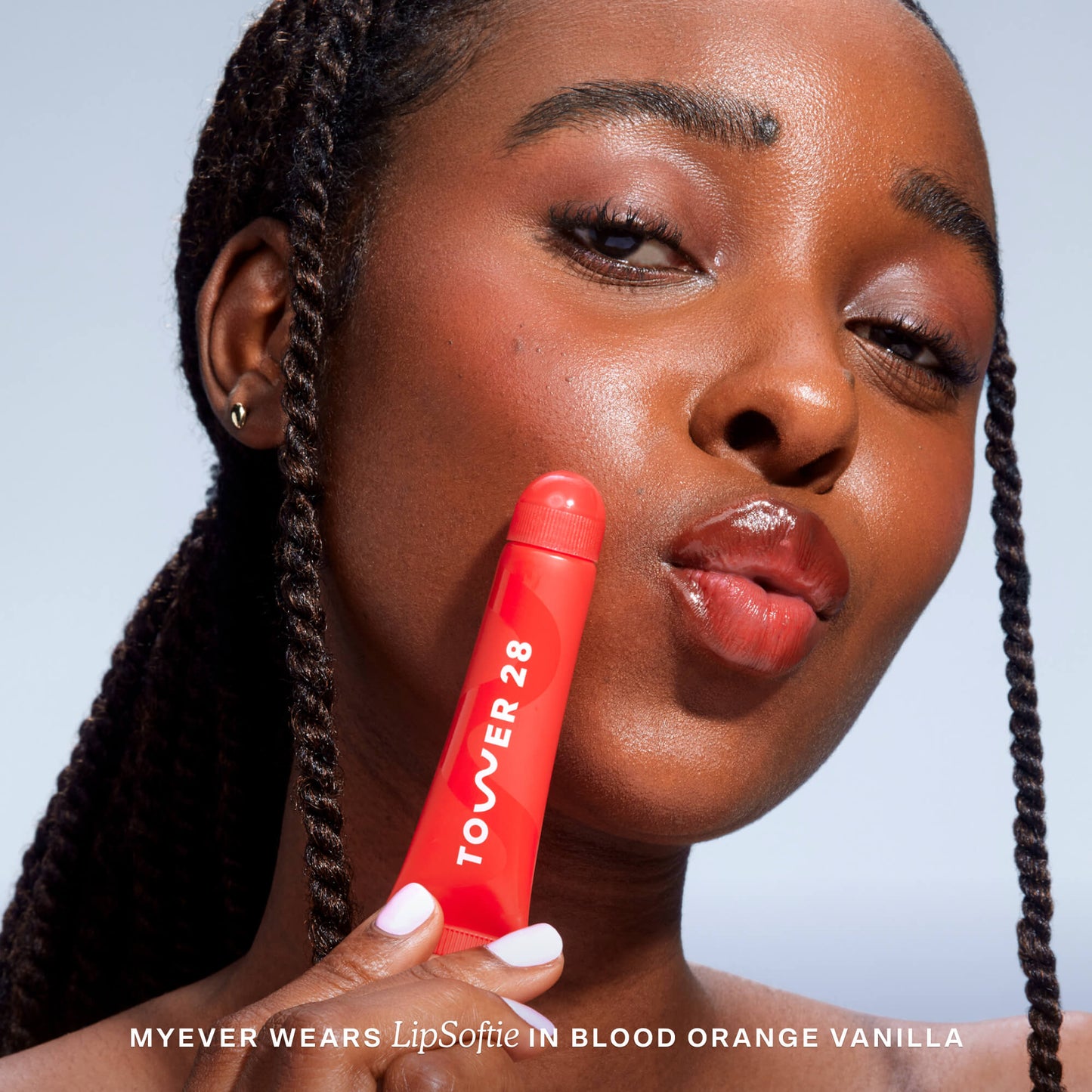 Blood Orange Vanilla [A close up of a model holding Tower 28 Beauty's LipSoftie™ Lip Treatment in Blood Orange Vanilla and wearing it on her lips]