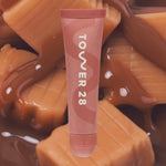 Lip balm tube with 'Tower 28' branding on a caramel background [Iced Dulce de Leche]