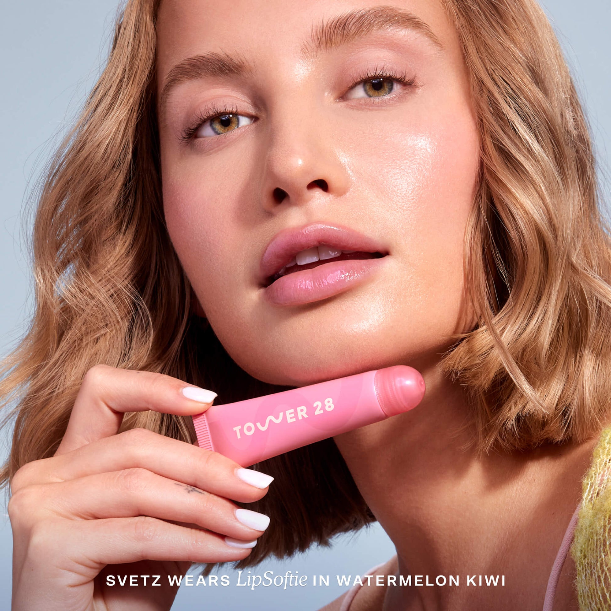 [Shared: A close up of a model holding Tower 28 Beauty's LipSoftie™ Lip Treatment in Watermelon Kiwi and wearing it on her lips