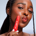 A close up of a model holding Tower 28 Beauty's LipSoftie™ Lip Treatment in Blood Orange Vanilla and wearing it on her lips. [Blood Orange Vanilla]