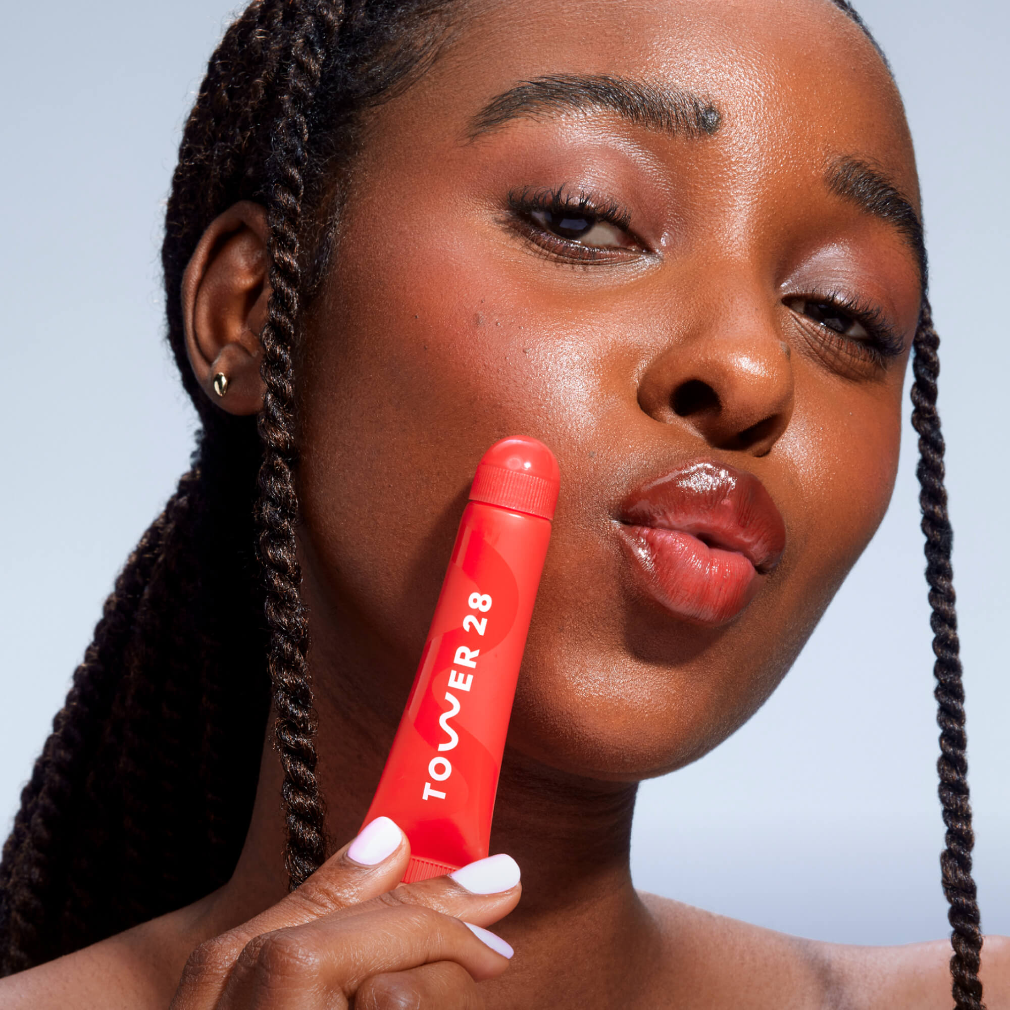 A close up of a model holding Tower 28 Beauty's LipSoftie™ Lip Treatment in Blood Orange Vanilla and wearing it on her lips. [Blood Orange Vanilla]