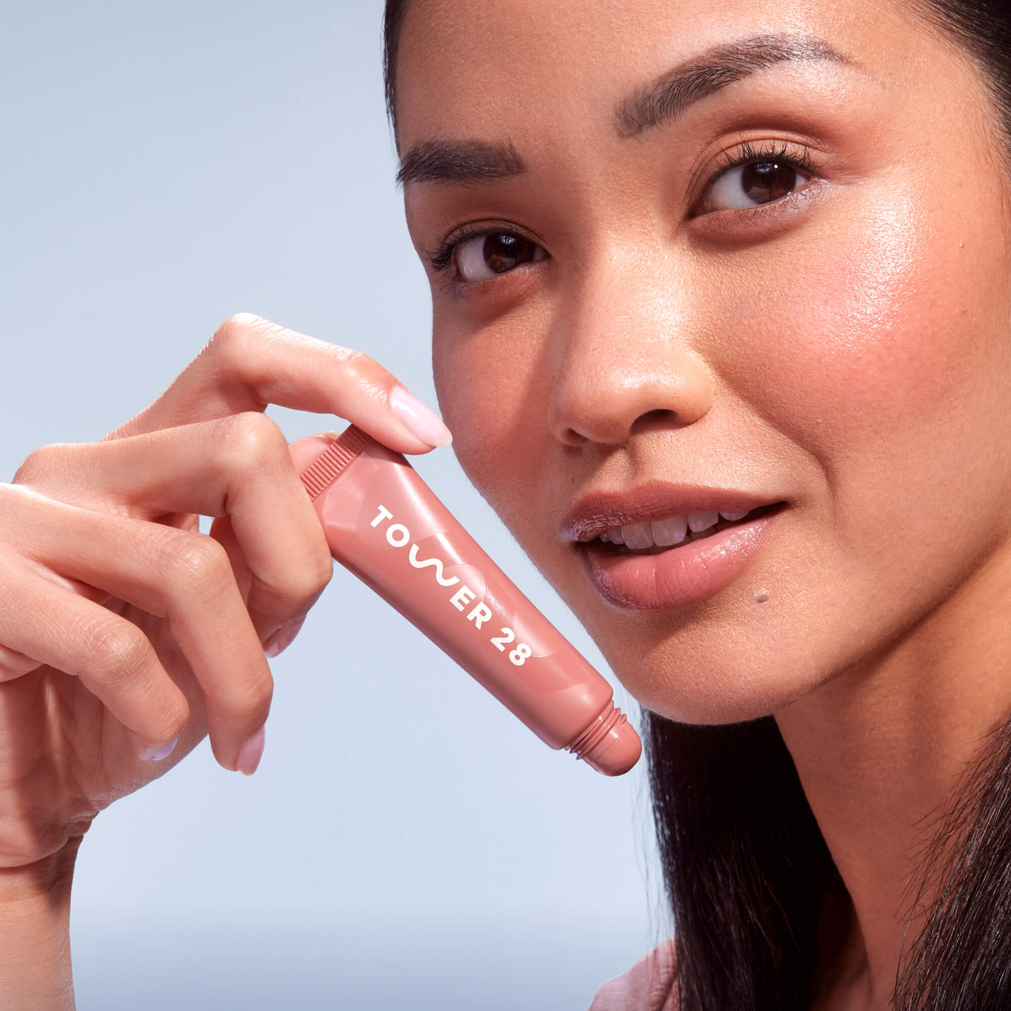 A close up of a model holding Tower 28 Beauty's LipSoftie™ Lip Treatment in Dulce de Leche and wearing it on her lips. [Dulce de Leche]