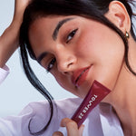 A close up of a model holding Tower 28 Beauty's LipSoftie™ Lip Treatment in Ube Vanilla and wearing it on her lips. [Ube Vanilla]