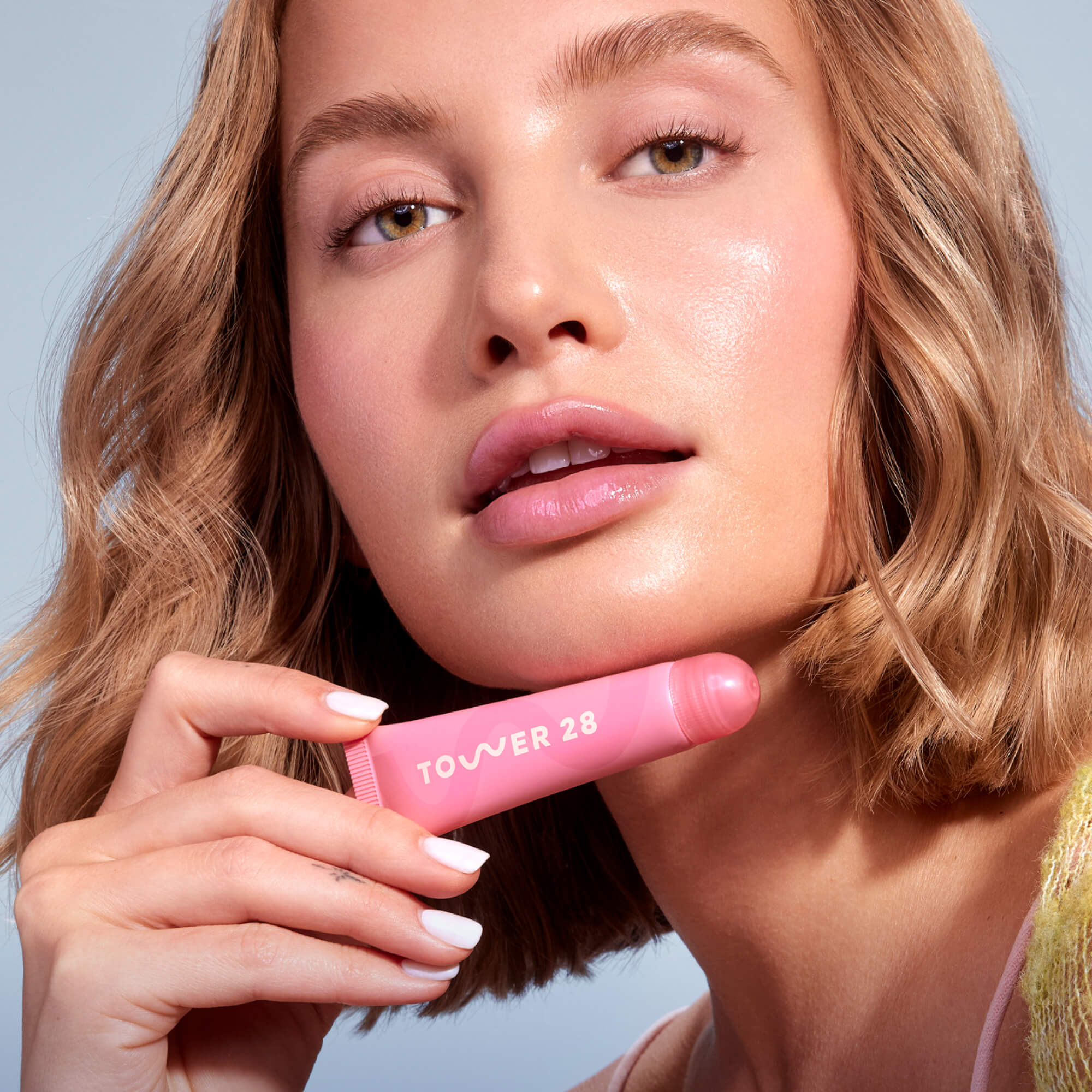 A close up of a model holding Tower 28 Beauty's LipSoftie™ Lip Treatment in Watermelon Kiwi and wearing it on her lips. [Watermelon Kiwi]