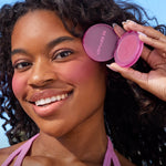 A person holds Tower 28 Beauty’s GetSet Powder Blush in the shade Pali Punch with a swatch of lavender pigment on their cheek. [Pali Punch]