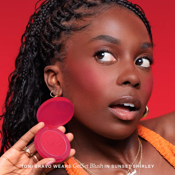 Woman holding a pink makeup compact with a red background [Sunset Shirley x Toni Bravo]
