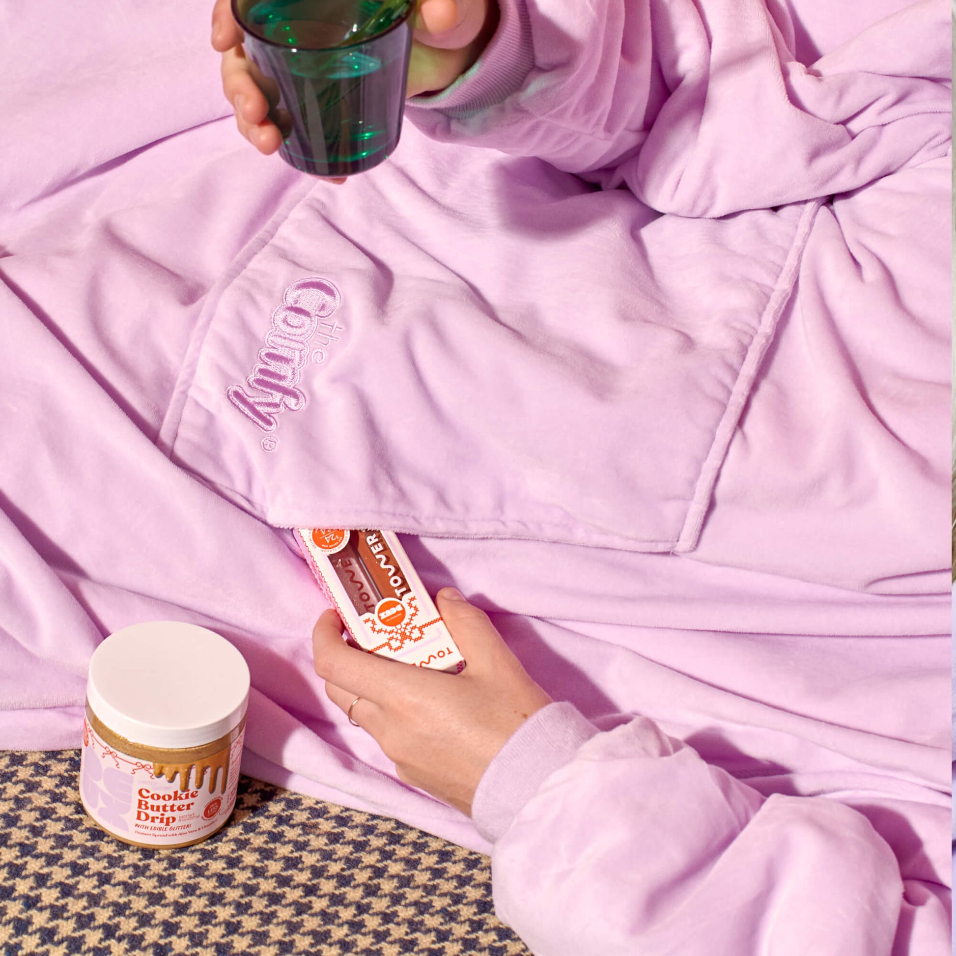 [Shared: A model lounging in Tower 28 Beauty x Comfy® Originals comfy alongside her Tower 28 Beauty x Deux Cookie Butter Drip and Lip Drip Duo, which features two full-sized ShineOn Lip Jelly.
