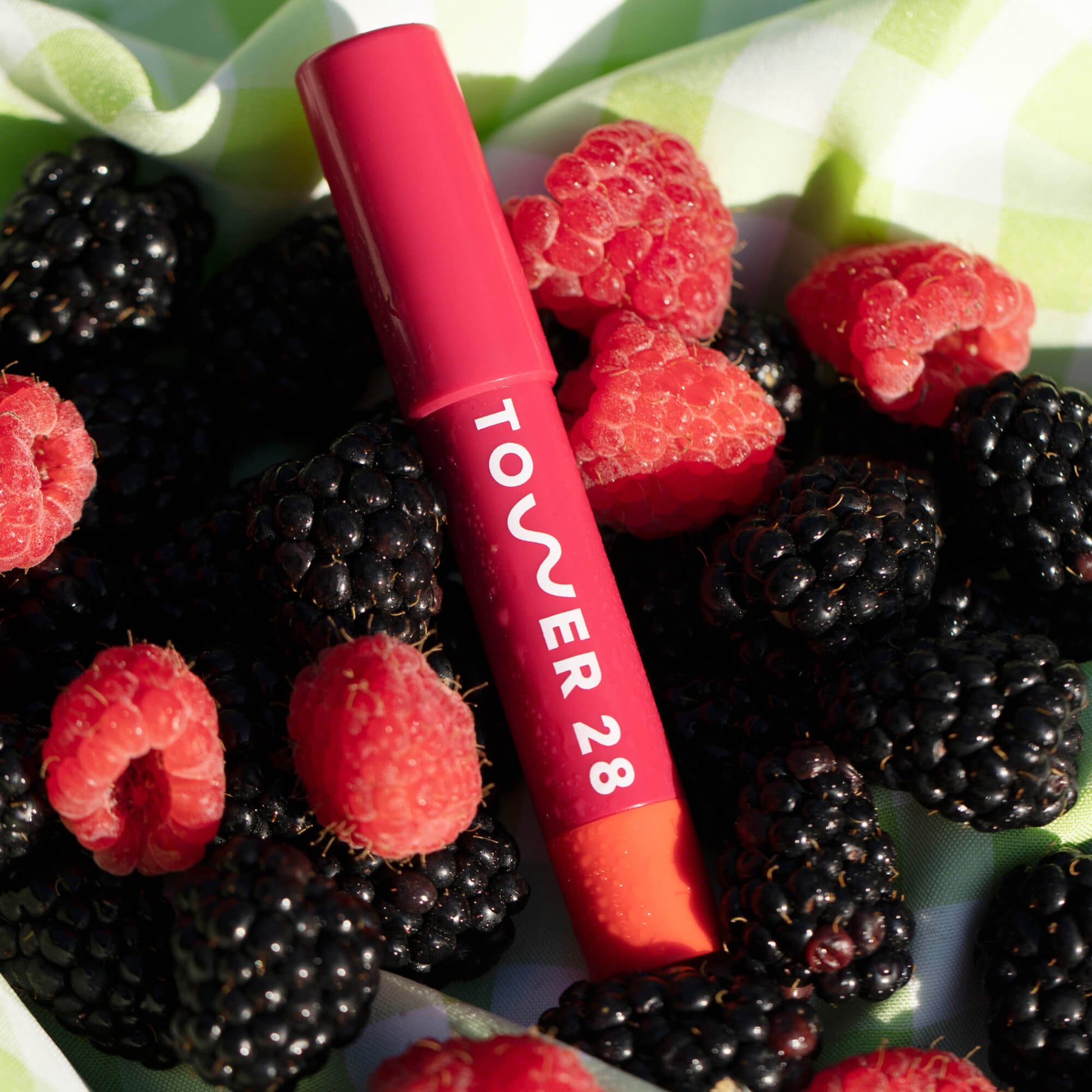 A close up of Tower 28 Beauty's JuiceBalm in shade Drink laying on top of berries