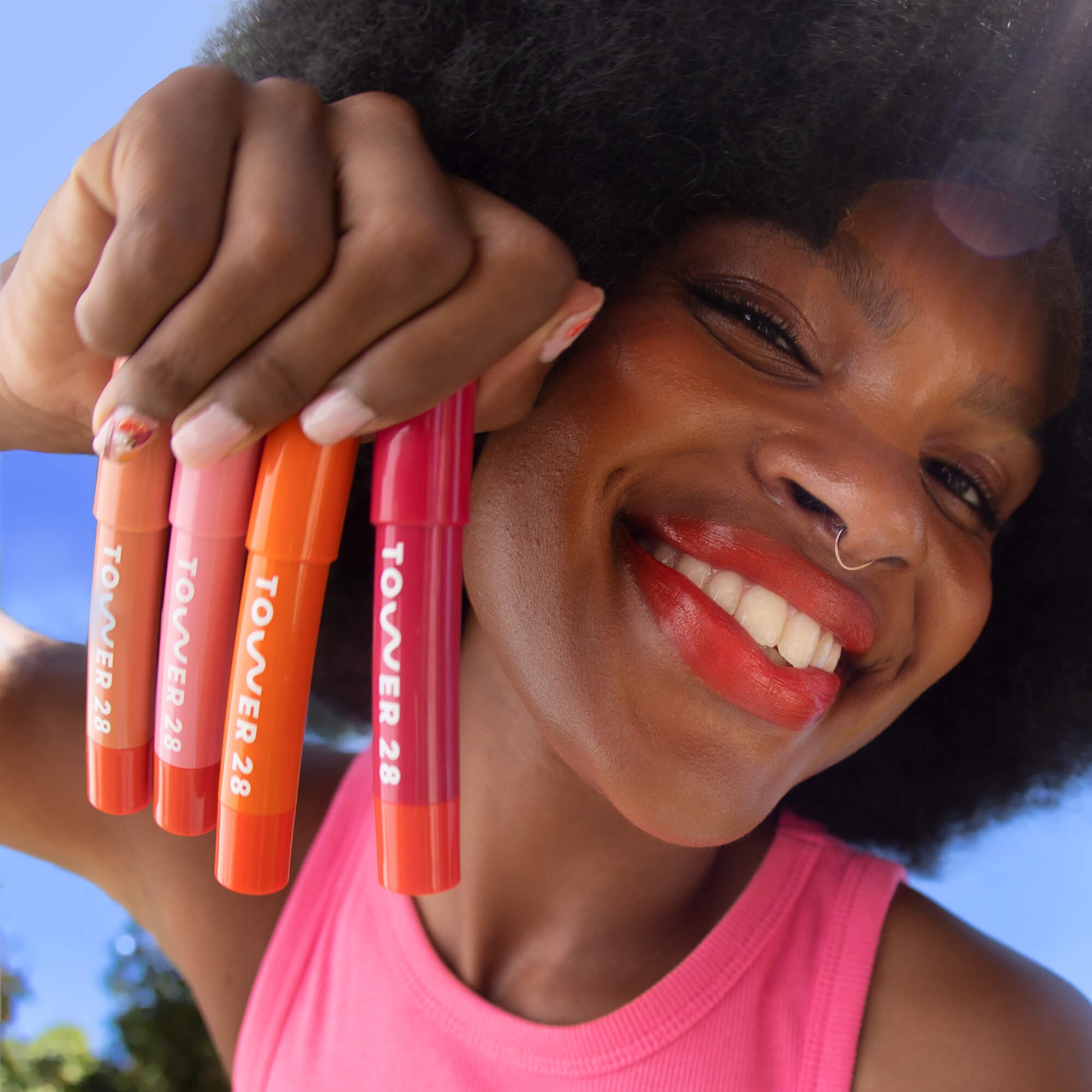 Shared: A model holding all four shades of Tower 28 Beauty's JuiceBalm in her hands: Drink, Shake, Mix, and Squeeze).