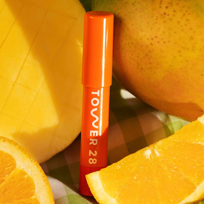 Shade: Squeeze [A close up of Tower 28 Beauty's JuiceBalm in shade Squeeze laying on top of lemons]