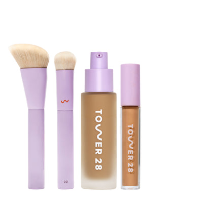 [shared] Tower 28 makeup set featuring a lavender brush, sponge, foundation bottle, and liquid foundation tube on a white background.