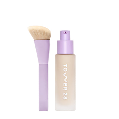 [shared] Tower 28 liquid foundation bottle in a frosted beige finish with a lavender pump, shown next to a matching lavender makeup brush with beige bristles on a white background.