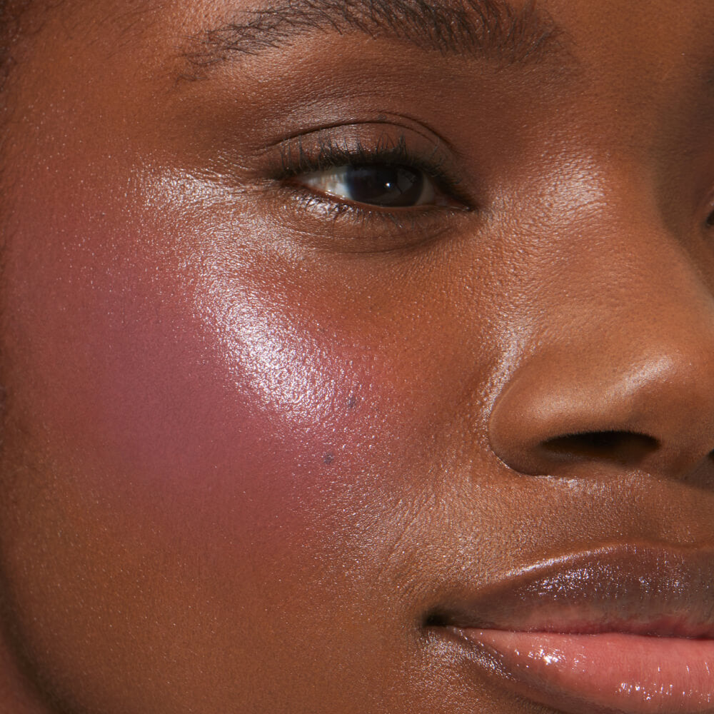 A close-up of a model with medium skin tone wearing Tower 28 Beauty's BeachPlease Cream Blush in Party Hour