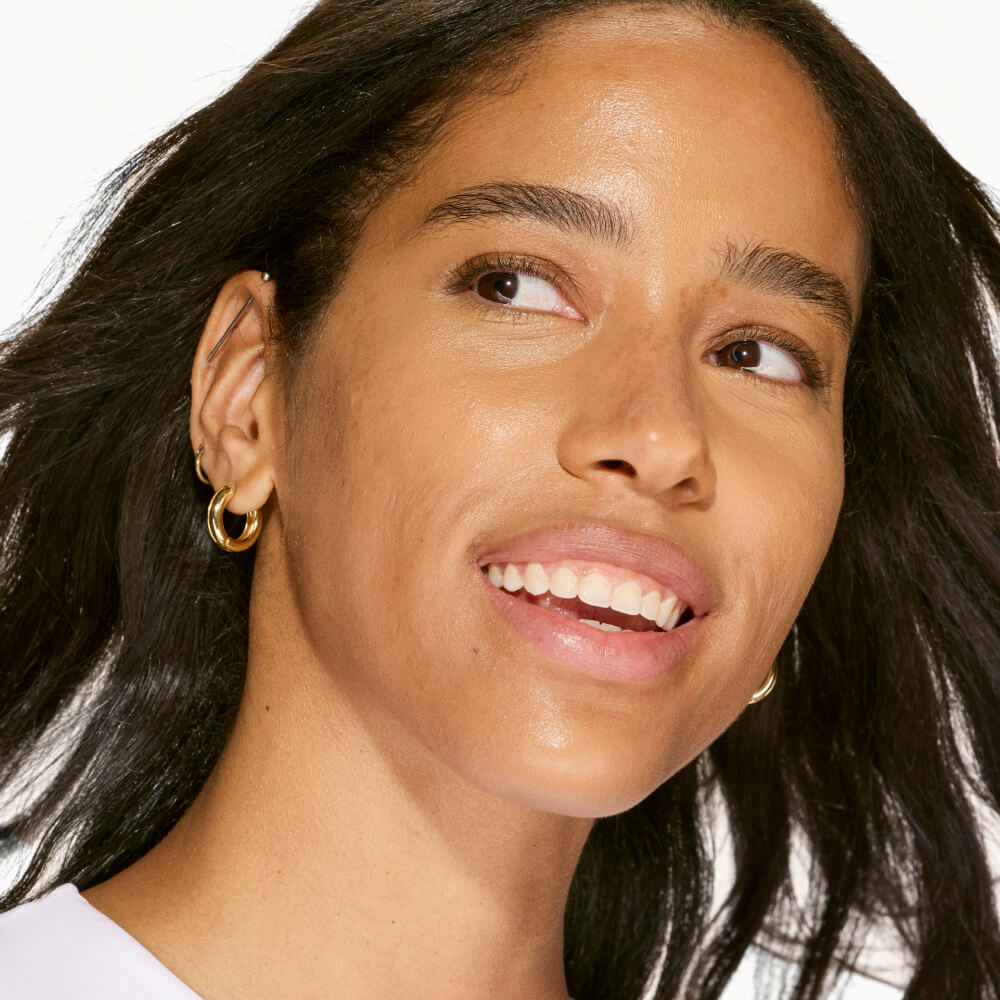 A person shown wearing Tower 28 Beauty's Swipe Serum Concealer in 13.0 PLAYA, with evened skin tone, smoothed texture, and natural-looking coverage. [13.0 PLAYA]