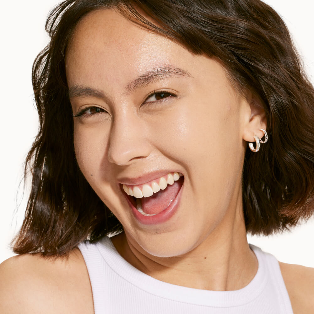 A person wearing Tower 28 Beauty's Swipe Serum Concealer in shade 5.0 EP, shown with an even-toned, radiant complexion and natural glow. [5.0 EP]