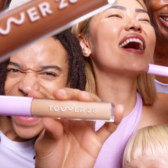 [A close up of two models holding the Tower 28 Beauty Swipe Serum Concealer in different shades.]