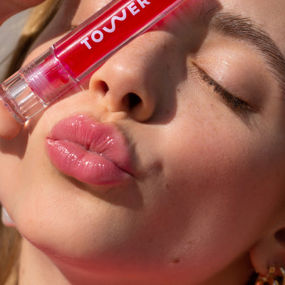 [A close up of a model wearing the Tower 28 Beauty ShineOn Lip Jelly in XOXO and holding the product next to her face.]