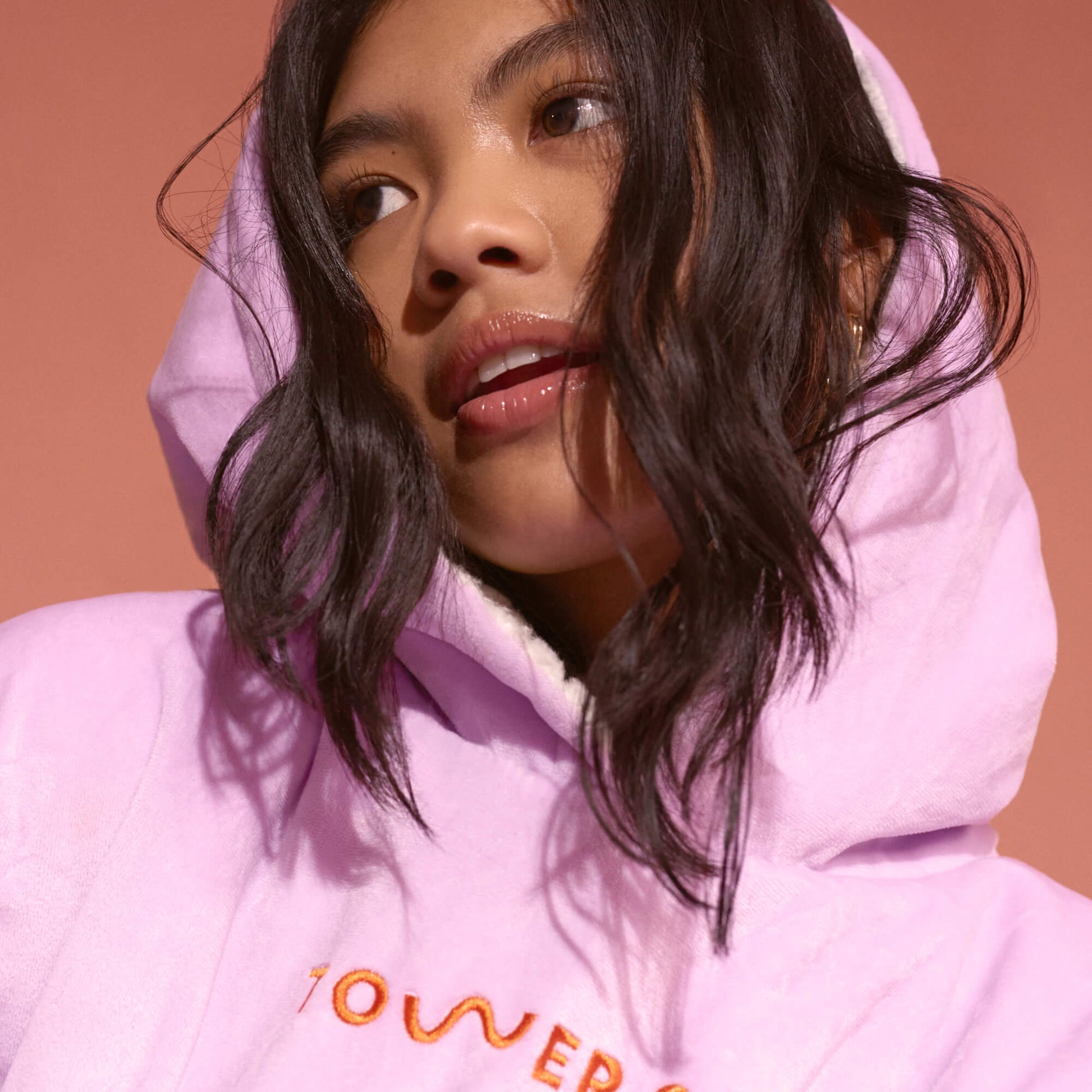 [Shared: A model wearing her Tower 28 Beauty x Comfy® Originals comfy, which is in a light purple with an orange logo placed across the chest.