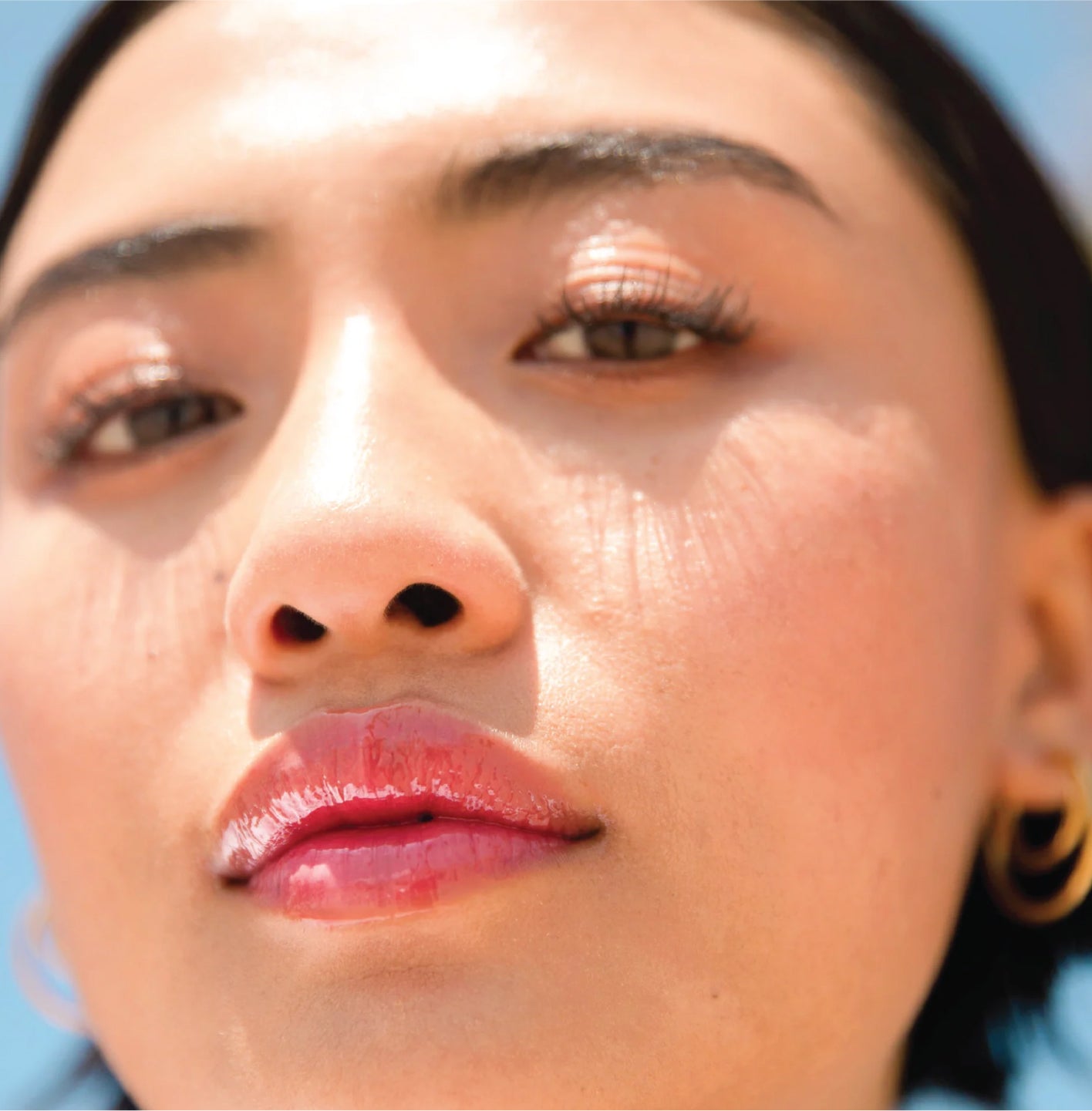 A closeup of a model with glossy lips wearing the Tower 28 Beauty ShineOn Lip Jelly.