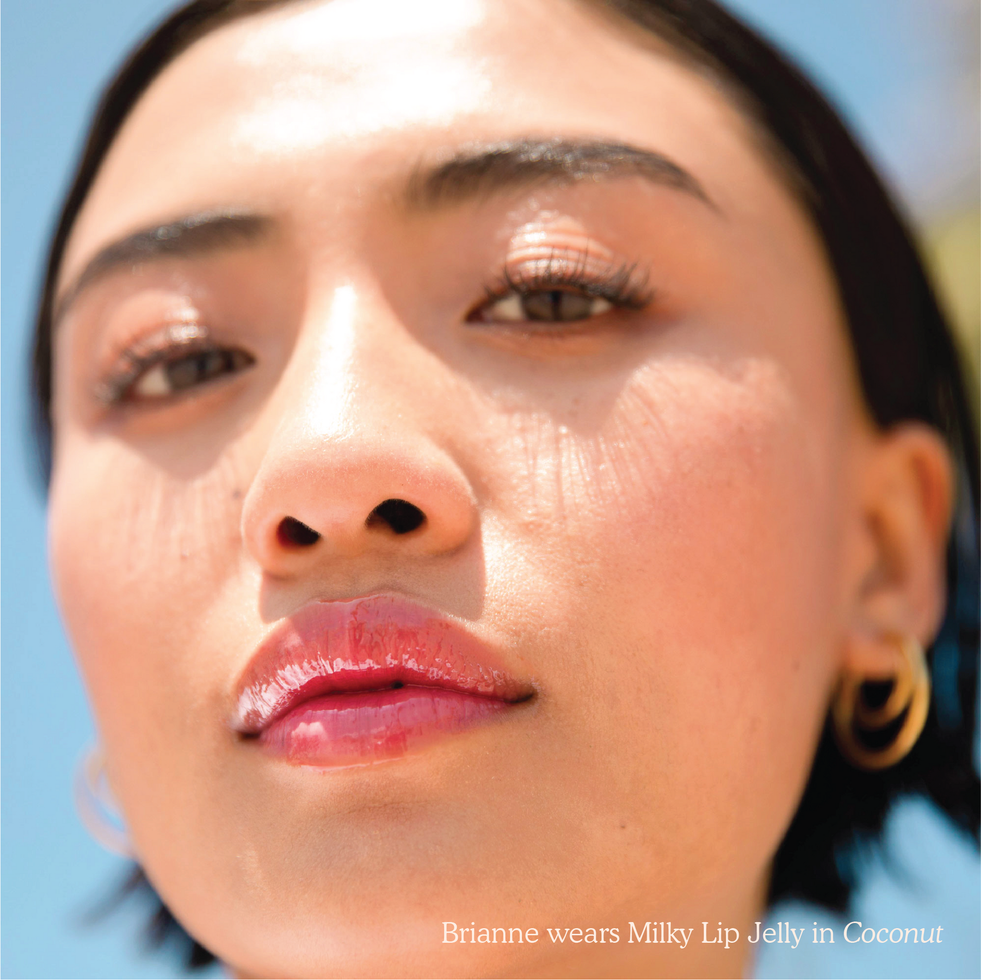 Closeup photo of a girl with very glossy lips, wearing the Tower 28 Beauty ShineOn Milky Lip Jelly shade in Coconut (a milky mauve-pink)